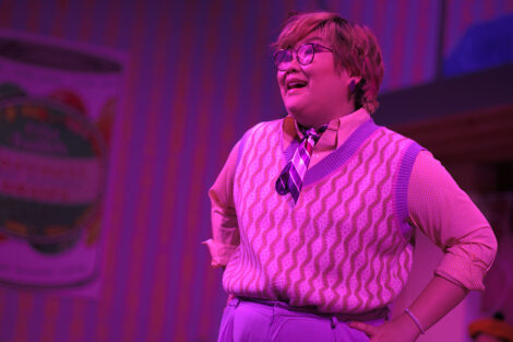 students in a stage production act on stage with pink dramatic lighting