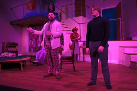 students in a stage production act on stage with pink dramatic lighting