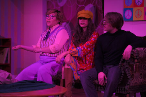 students in a stage production act on stage with pink dramatic lighting