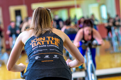 student rides a spin bike, her tank says 