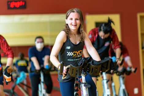 Perry Zimmerman smiles as she rides a spin bike, other students on spin bikes behind her