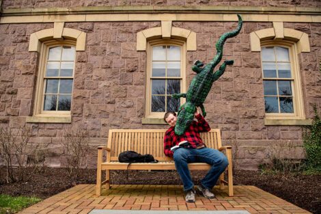 Student sits on bench reading while an alligator bites his shoulder