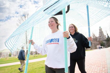 Two students hold blue poles to support what looks like a large umbrella