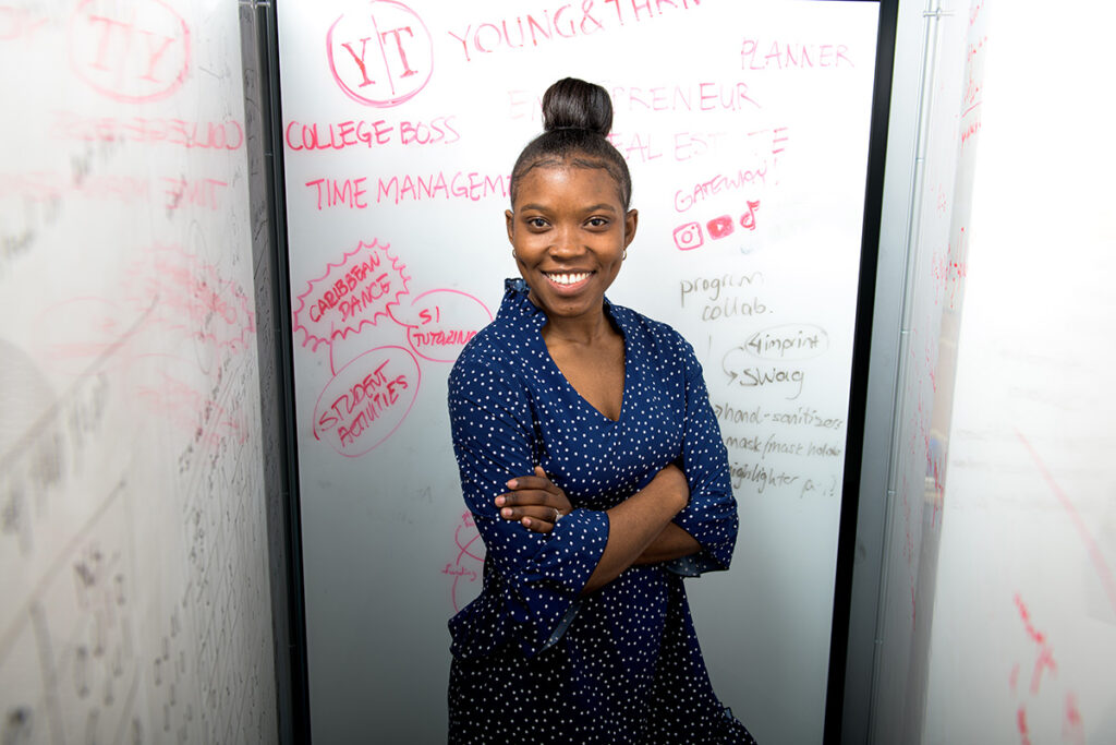 Shantae Shand smiles with her arms crossed, in front of a whiteboard filled with red writing.