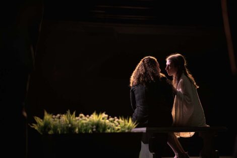 Two women sit on a bench and talk intimately