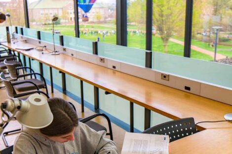 student studies at a desk in Skillman, a colorful hot air balloon is visible through a window