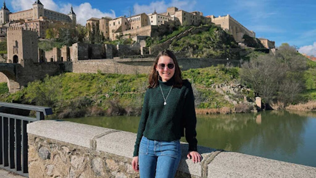 Class of 2022 valedictorian Madeline Carroll leaning against a stone wall in front of a picturesque landscape