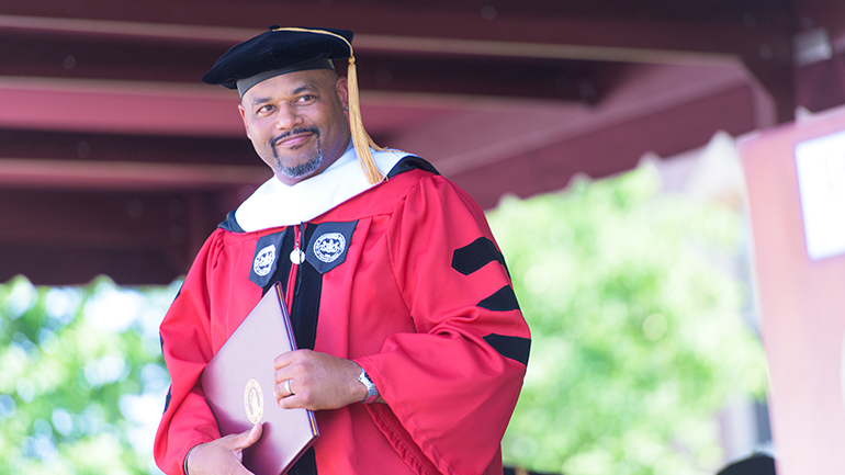 Harrison Bailey smiles holding a degree and in cap and gown