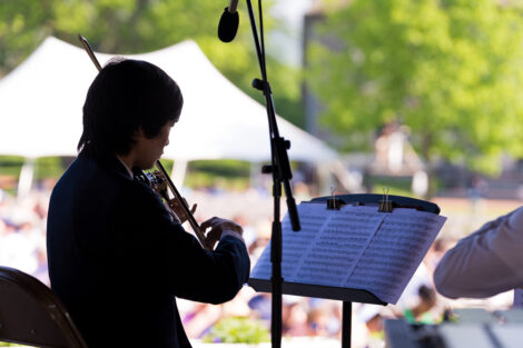 student plays the violin, crowd of people look on from Quad