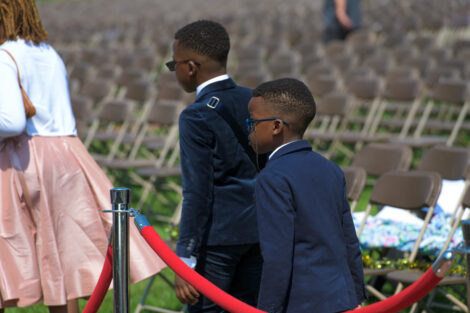 two small children in suits walk past red rope