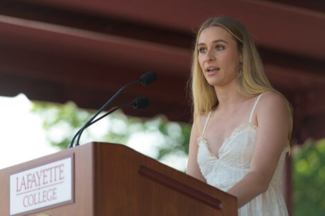 student in white dress stands at podium and talks