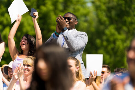 student in crowd stands and smiles and claps