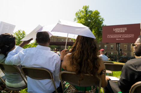 family members sit under umbrella to watch ceremony on stage