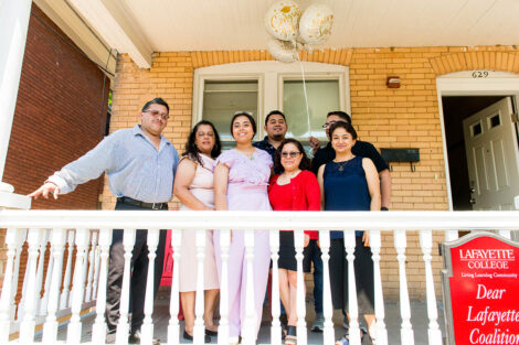 student stands on porch with family members and celebratory balloons
