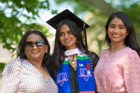 student stands between family members in cap and gown and smiles