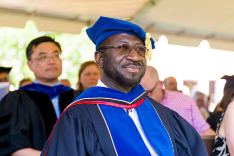Rex Ahene in cap and gown sits under a tent
