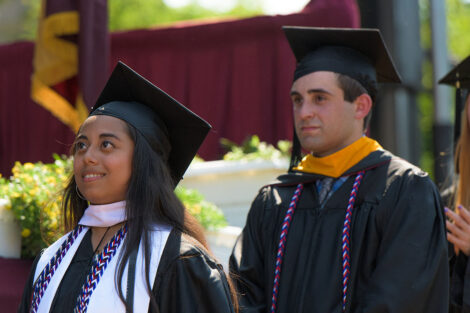 students in caps and gowns smile as they wait to climb up to the commencement stage