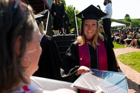 student in cap and gown smiles and receives diploma