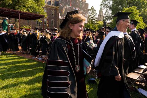 Nicole Hurd and Chip Bergh walk in caps and gowns across grass