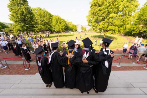 group of grads in caps and gowns stand together on steps of Skillman with view of the Quad in front of them
