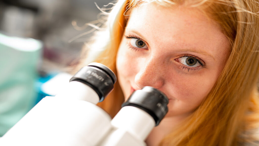 Samantha Ganser '23 looks up from a microscope while working in Prof. Justin Hines' lab