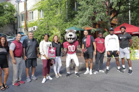 Lafayette College President Nicole Hurd, head football coach John Troxell, football team members, and Leopards mascot standing on a Downtown Easton Street with a restaurant in the background