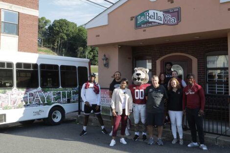 Lafayette College President Nicole Hurd, head football coach John Troxell, football team members, and Leopards mascot standing in front of La Bella Via Restaurant