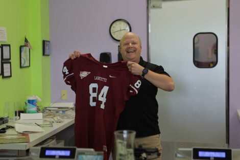 Owner of Just a Dream frozen yogurt shop holding up a Lafayette football jersey and smiling