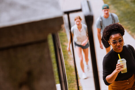 A student drinks a coffee walking up a flight of stairs.