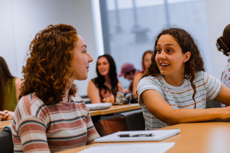 Two students talk in a classroom.