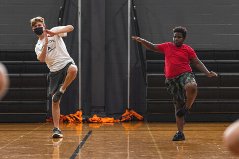 a Lafayette student and a young Easton student balance while doing a yoga pose in a gymnasium