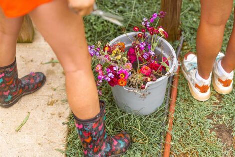 a bucket of wildflowers sits on the ground, the feet of two students are visible next to it