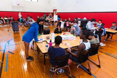 a Lafayette student leans on a table where school children sit
