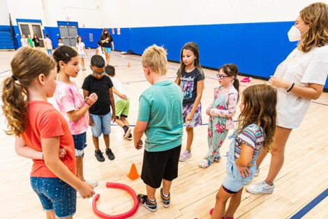 a group of school-aged children gather together in a gymnasium with a Lafayette student