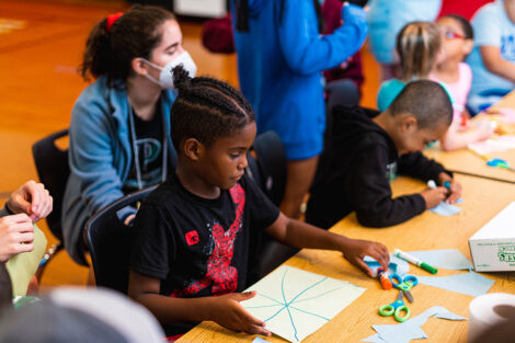 young students sit at a table and color with markers
