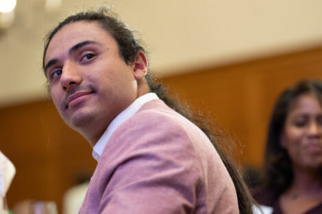 Marco Olivas is wearing a pink jacket and is looking over his shoulder.