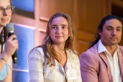 Colleen McNamara is wearing a tan jacket and is on the stage with fellow students during the discussion.