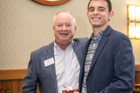 Alumni Association Board President Michael Weisburger '82 is standing next to Tyler Osipower '24, who is holding a leopard wrapped gift.