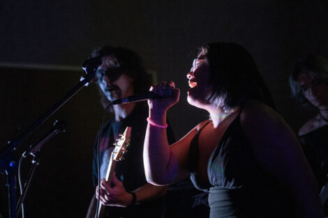 A student sings into a microphone during a performance at the LGBTQIA+ formal.